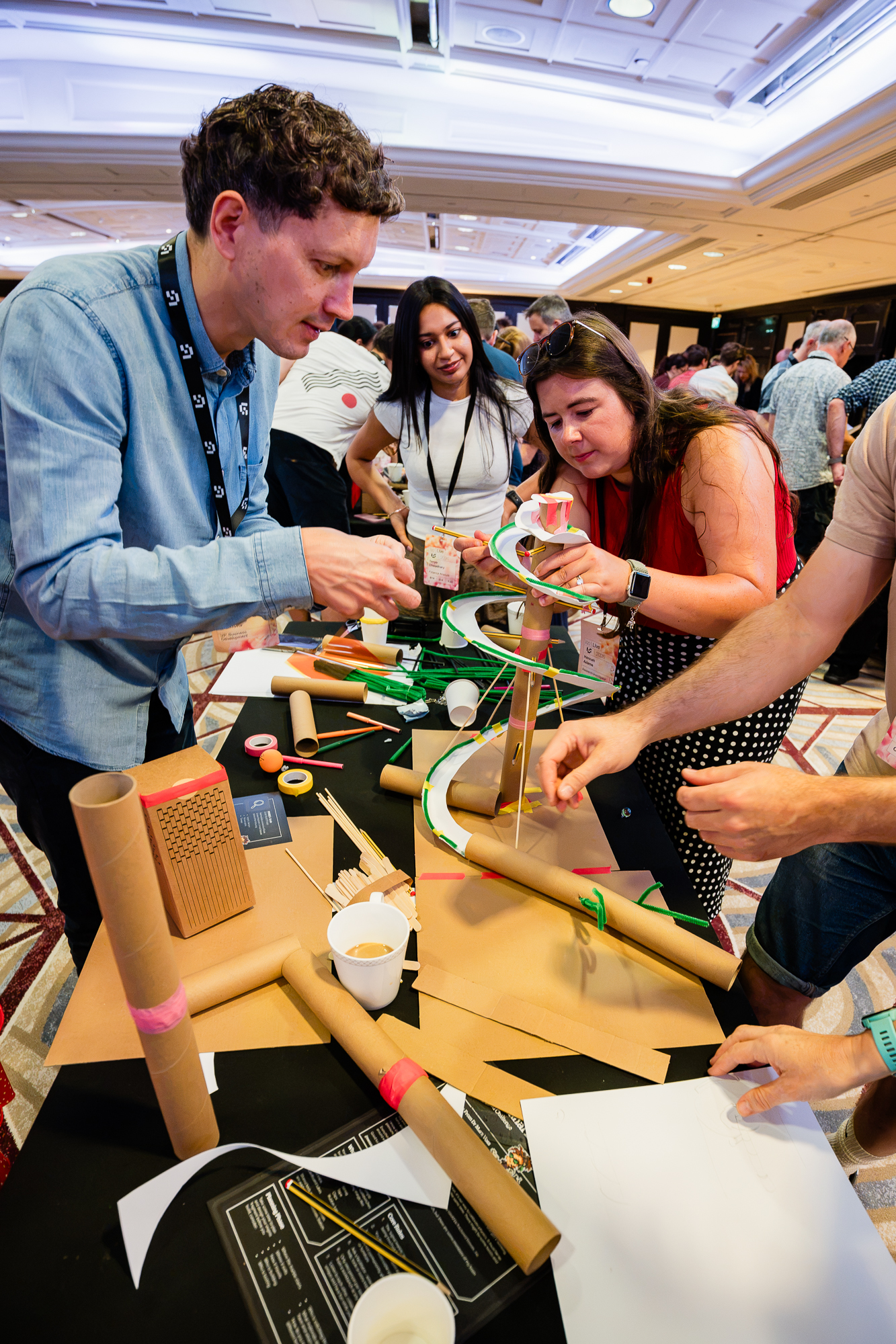 Colleagues focused on a colourful marble run build with green rubber bands, paper spirals and cardboard tubes.